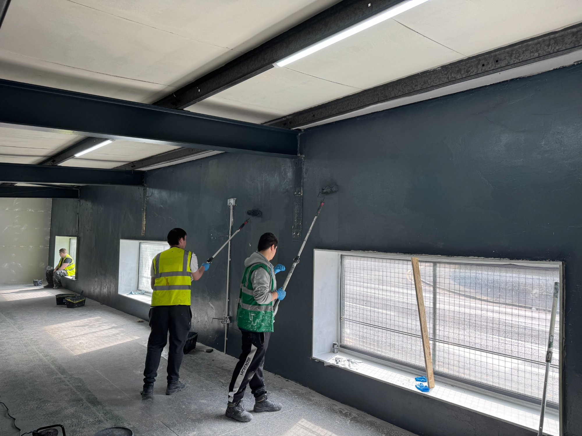 Two volunteers painting the long gym wall