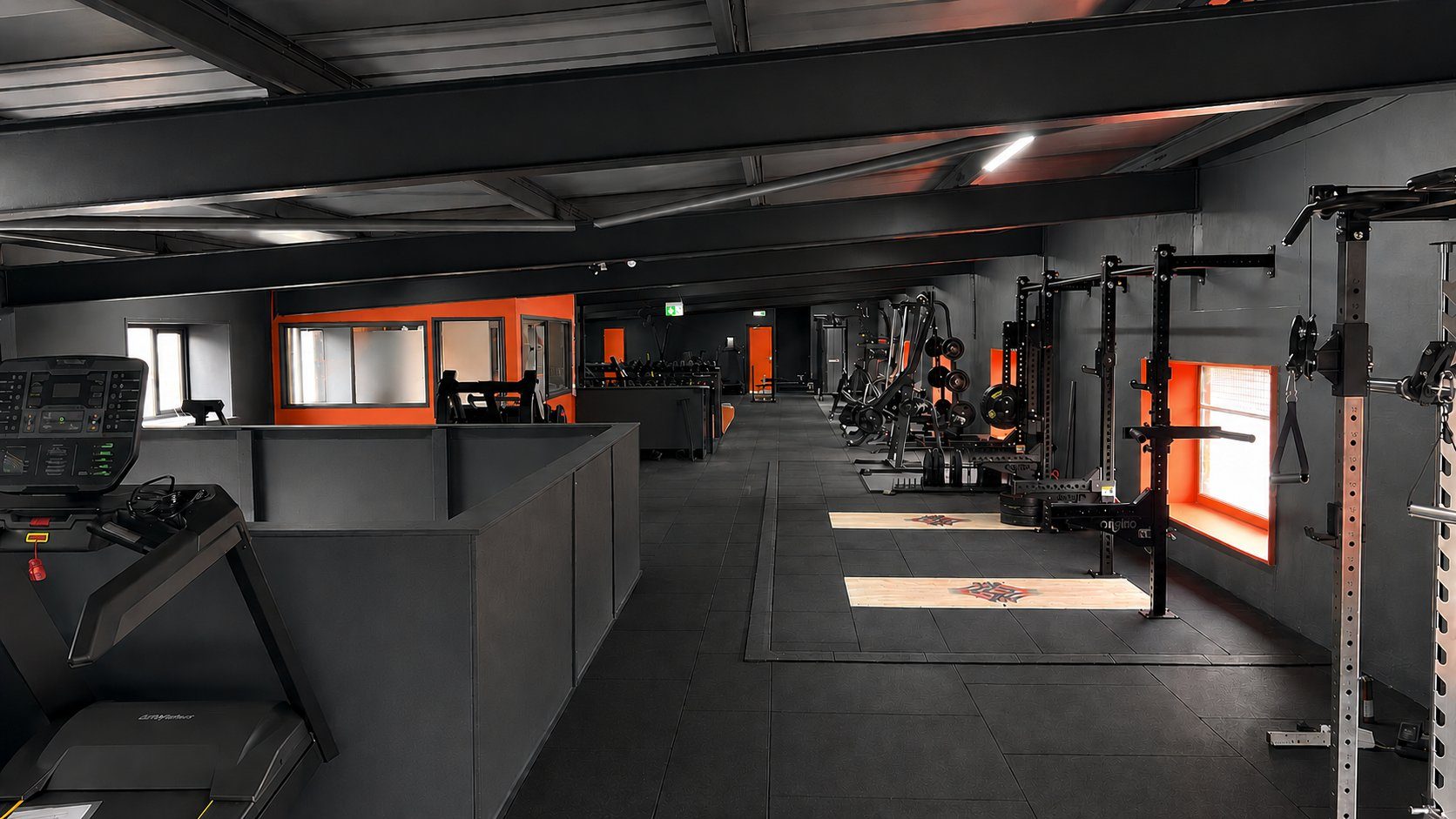 The gym floor at Legacy HQ — racks, plates and cardio kit under the mill's steel beams
